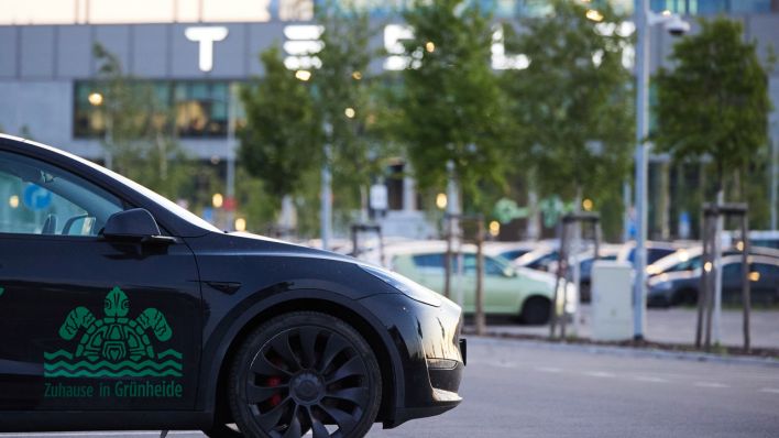Ein Tesla, auf dem eine Schildkröte und der Spruch "Zuhause in Grünheide" steht, steht vor dem Tesla-Werk.