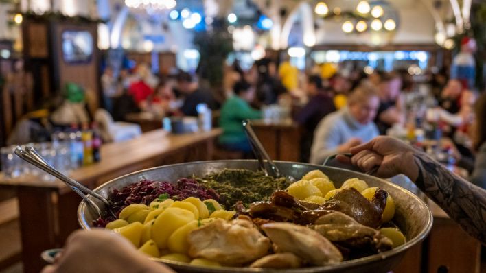 Eine Kellnerin trägt im Hofbräu Berlin bei einem Weihnachtsessen eine Pfanne zum Tisch.