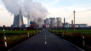 Eine Straße führt auf das Kohlekraftwerk Niederaußem mit seinen großen Kühltürmen hin.