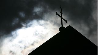 Eine Kirchturmspitze im Gegenlicht und vor wolkenverhangenem Himmel (Bild: DPA)