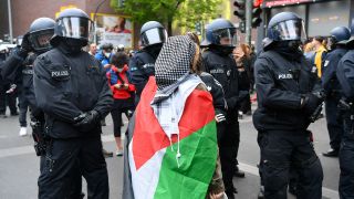 Symbolbild:Einsatzkräfte der Polizei und eine Demo-Teilnehmerin mit einer Palästina-Flagge um den Körper geschlungen.(Quelle:dpa/P.Zinken)