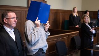 17.10.2023, Berlin: Eine Krankenschwester, die in einem Fall von Totschlag wegen Beihilfe angeklagt ist,hält sich zu Prozessbeginn einen Aktenordner vor das Gesicht.(Quelle:dpa/S.Gollnow)