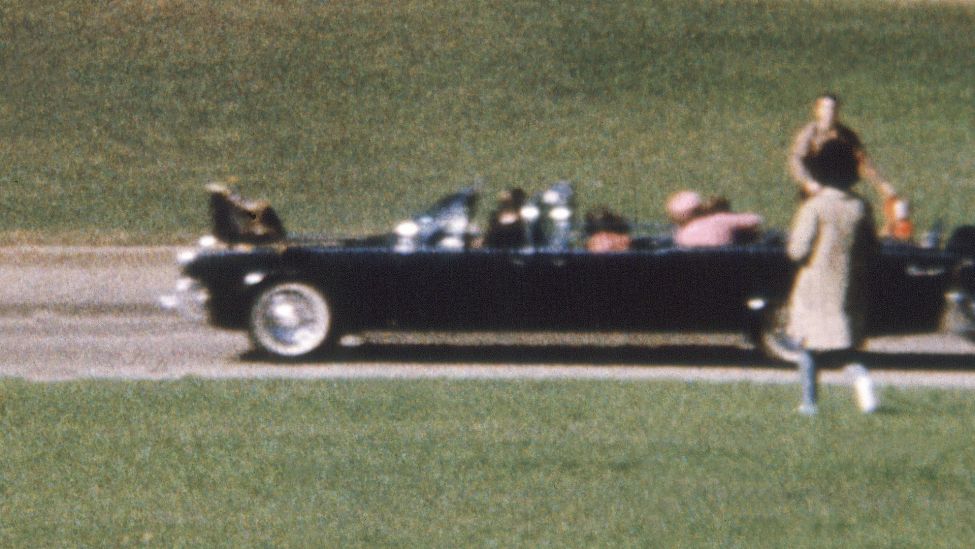 Nach den tödlichen Schüssen auf ihren Mann, den US-Präsidenten John Fitzgerald Kennedy, legt Jacqueline Kennedy (rosa Kostüm) ihren Arm um ihn, um seinen Körper zu stützen. Ein Amateur machte die Aufnahmen von der Ermordung Kennedys in Dallas/Texas am 22. November 1963 (Quelle: dpa / UPI).