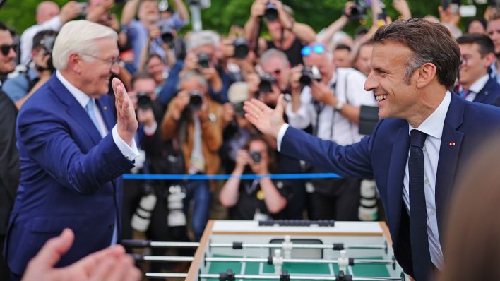 Emmanuel Macron, Präsident von Frankreich, besucht zusammen mit Bundespräsident Frank-Walter Steinmeier das Demokratiefest aus Anlass von 75 Jahren Grundgesetz und sie stehen dabei an einem Tischkicker. (Quelle: Picture Alliance/Kay Nietfeld)