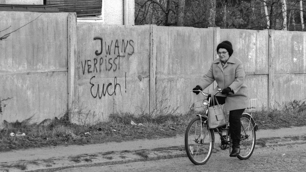 Eine alte Dame fährt 1990 mit dem Fahrrad an der der Kasernen-Mauer in Wünsdorf, Brandenburg vorbei. "Iwans verpisst euch", Spruch an der Mauer. (Quelle: dpa/SZ Photo/Paul Glaser)