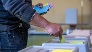 Ein Mann wirft seine Stimzettel in die Wahlurne, um seine Stimmen abzugeben. In Rheinland-Pfalz findet Kommunalwahlen und die Europawahl am selben Tag statt. (Quelle: dpa/Harald Tittel)