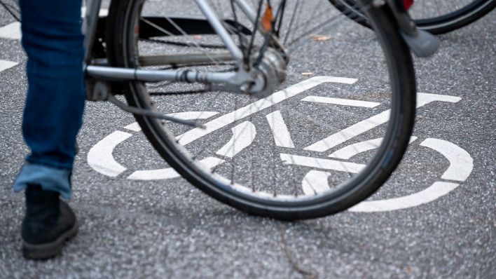 Symbolbild: Ein Fahrrad-Symbol ist auf der Fahrbahn einer Straße hinter einem Fahrrad zu sehen. (Quelle: dpa/Jonas Walzberg)