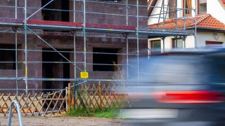 Symbolbild: Ein Auto fährt vorbei an einem nicht fertiggestellten neu gebauten Einfamilienhaus. (Quelle: dpa/Monika Skolimowska)