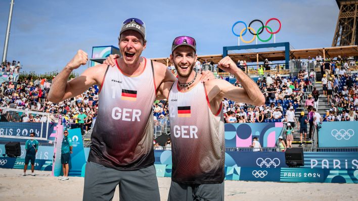 Die Beachvolleyballer Nils Ehlers (l.) und Clemens Wickler jublen vor den olympischen Ringen (Foto: imago images / Conny Kurth)