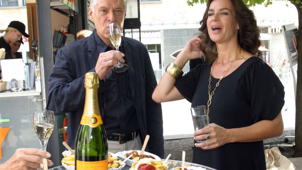 Die Eiskunstläuferin Katarina Witt und der Schauspieler Rüdiger Joswig stehen mit Champagner und Currywurst bei einem Pressetermin (Quelle: dpa/Xamax)