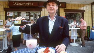 Schauspieler Harald Juhnke 1991 vor Konnopke's Imbisstand in Berlin mit Currywurst und einem Glas Berliner Weiße (Quelle: dpa/Günter Gueffroy).