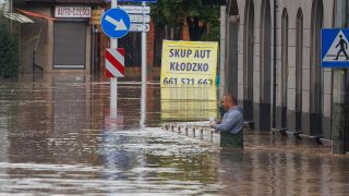 Ein Mann steht in hüfthohem Wasser, das nach tagelangem, ungewöhnlich starkem Regen die Straßen und Häuser überflutet hat. (Quelle: dpa/Krzysztof Zatycki)