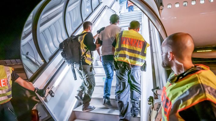 Symbolbild: Polizeibeamte begleiten einen Mann auf dem Flughafen in ein Charterflugzeug. (Quelle: dpa/Michael Kappeler)