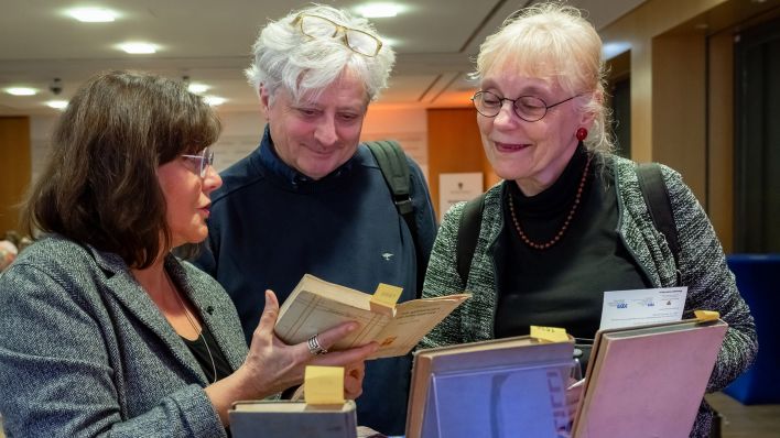 Die Historikerin und Provenienzforscherin Irena Strelow (l) zeigt Marc Mendelson (M), Nachfahre der Sportlerin Lilli Henoch, und dessen Ehefrau Sybille Knobloch (r) vor Beginn einer Veranstaltung in der Landesvertretung Sachsen-Anhalt in Berlin historische Bücher der Sportlerin (Quelle: dpa / Soeren Stache).