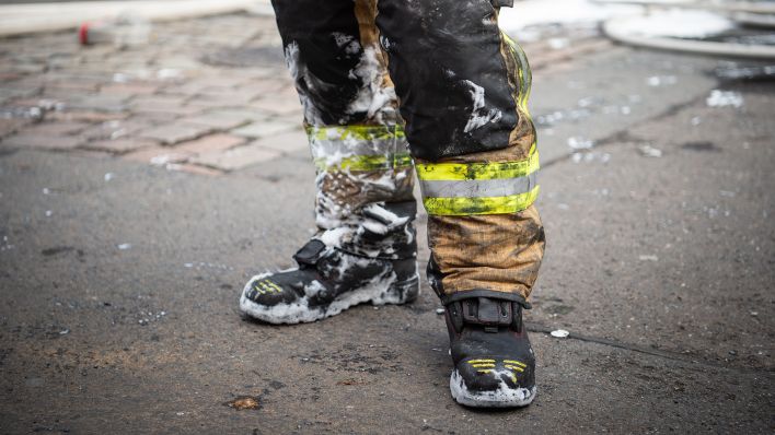 Symbolbild: : Ein Feuerwehrmann steht mit Schaum und Ruß verdreckter Kleidung nach einem Brandeinsatz. (Quelle: dpa/Arne Immanuel Bänsch)