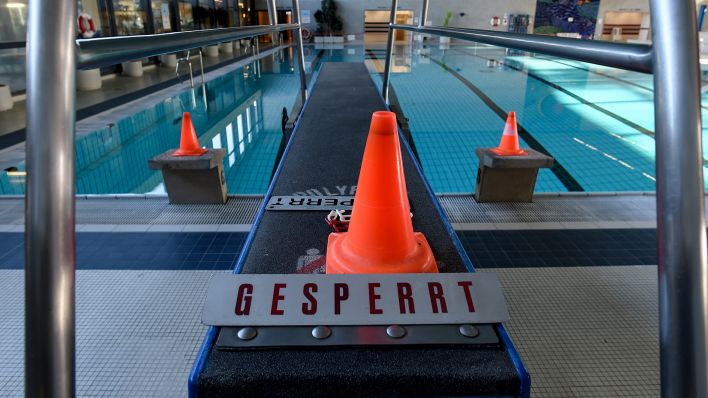 Symbolbild: Ein Sprungbrett mit Warnkegeln und einem Schild mit der Aufschrift "Gesperrt" vor dem leeren Becken. (Quelle: dpa/Hofmann)