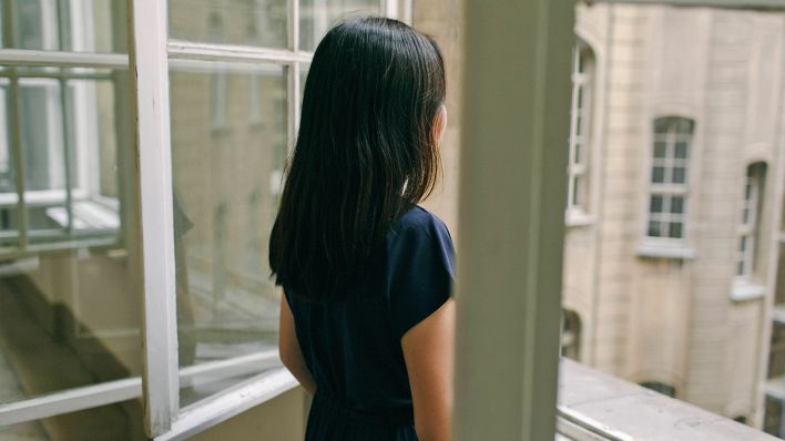 Symbolbild:Eine junge Frau schaut aus dem geöffneten Fenster.(Quelle:imago images/O.Guryanova)