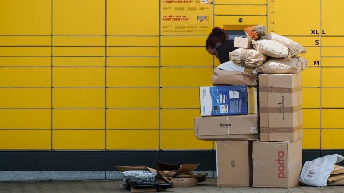 Symbolbild: Eine Paketzustellerin legt Pakete in eine Packstation, vor ihr steht ein großer Stapel. Bild: IMAGO / Frank Drechsler