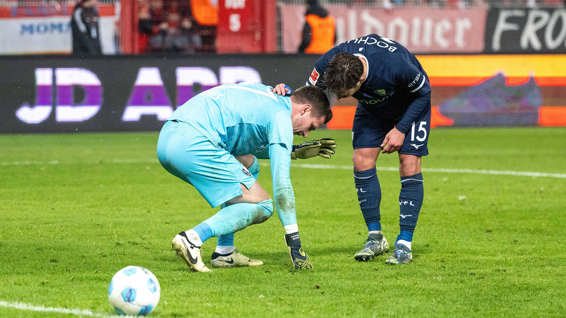 VfL-Bochum-Torhüter Patrick Drewes sinkt zu Boden, nachdem er im Bundesliga-Spiel beim 1. FC Union Berlin am 14.12.2024 von einem Feuerzeug getroffen wurde, Mitspieler Felix Passlack beugt sich über ihn (Bild: Imago Images/Matthias Koch)